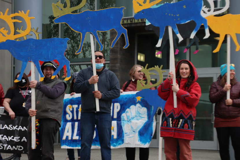 Protestors hold large signs shaped like caribou