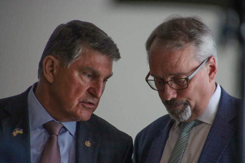 Joe Manchin leans over to speak in another man's ear
