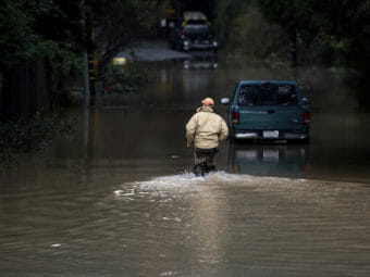 A man wading through knee-deep water in a road at night.