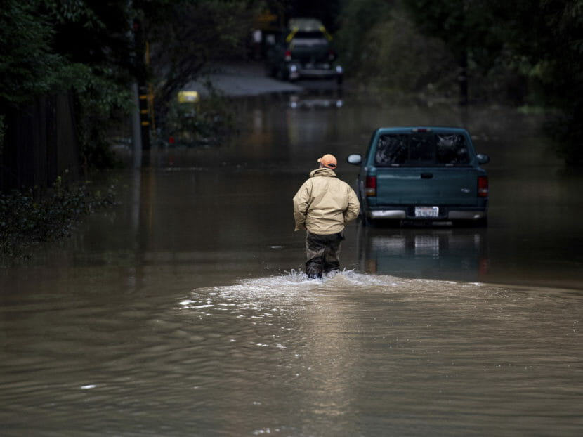 A man wading through knee-deep water in a road at night.