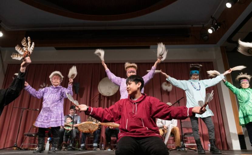 Dancers hold feathers as drummers play behind them