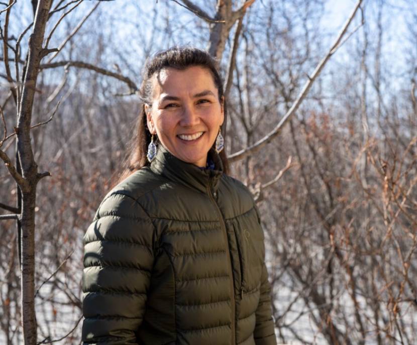 The candidate stands in front of leafless trees, with snow on the ground