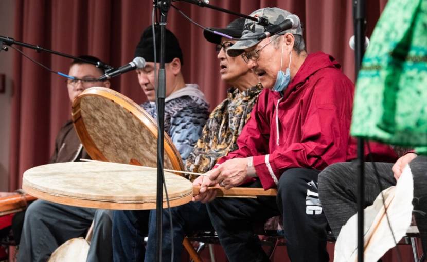 Four drummers, seated, playing skin drums on stage