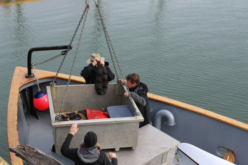 People unloading a large tote onto the deck of a ship