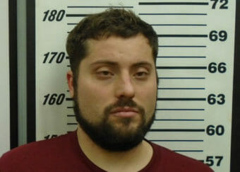 A mugshot of a man with dark hair and a beard