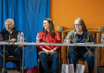 Three candidates sit at a table onstage.