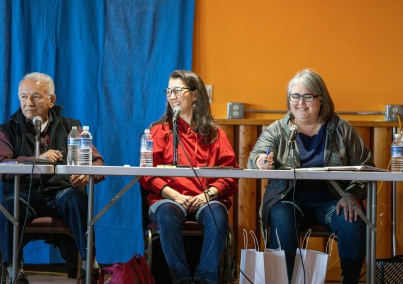 Three candidates sit at a table onstage.