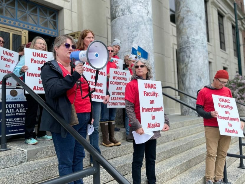 A woman speaks into a megaphone on the steps of the Alaska state capitol while others around her hold signs in support of university faculty