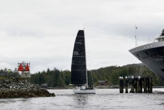 A sailboat slipping between shore and a cruise ship