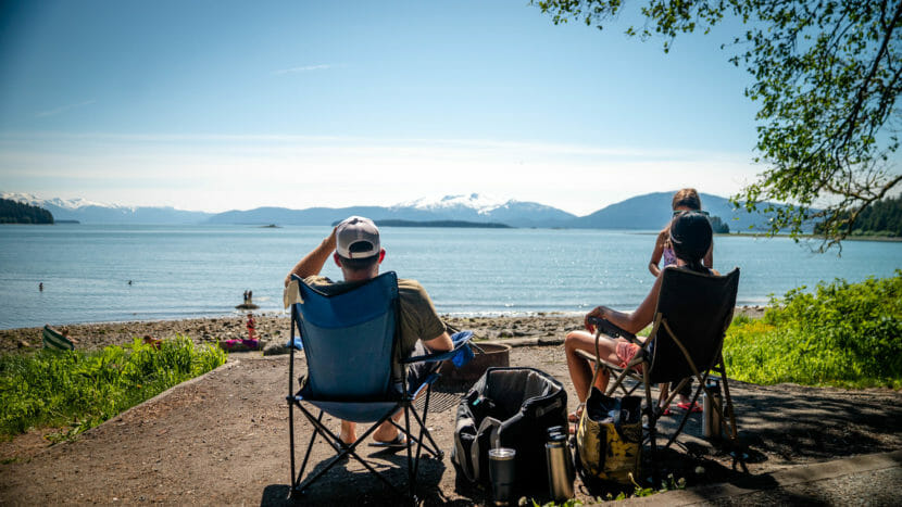 A couple, seen from behind, sitting on lawn chairs at the beach on a sunny day