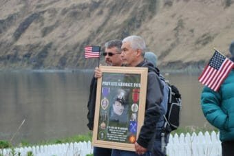 A man holds a framed photo of George Fox surrounded by images of his medals