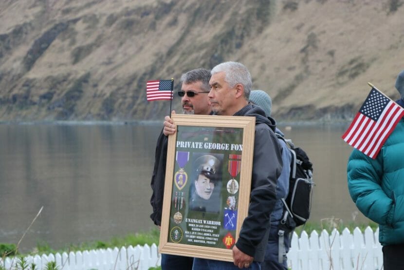 A man holds a framed photo of George Fox surrounded by images of his medals