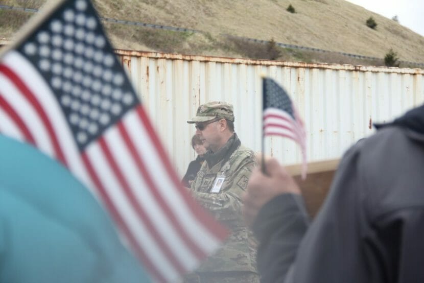 A man in uniform speaking with people holding American flags around him