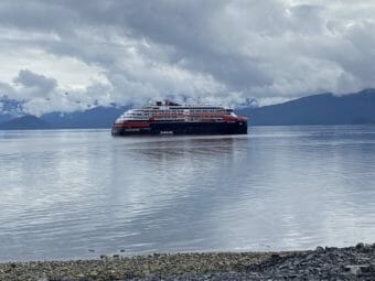 A cruise ship on calm waters with mountains behind it