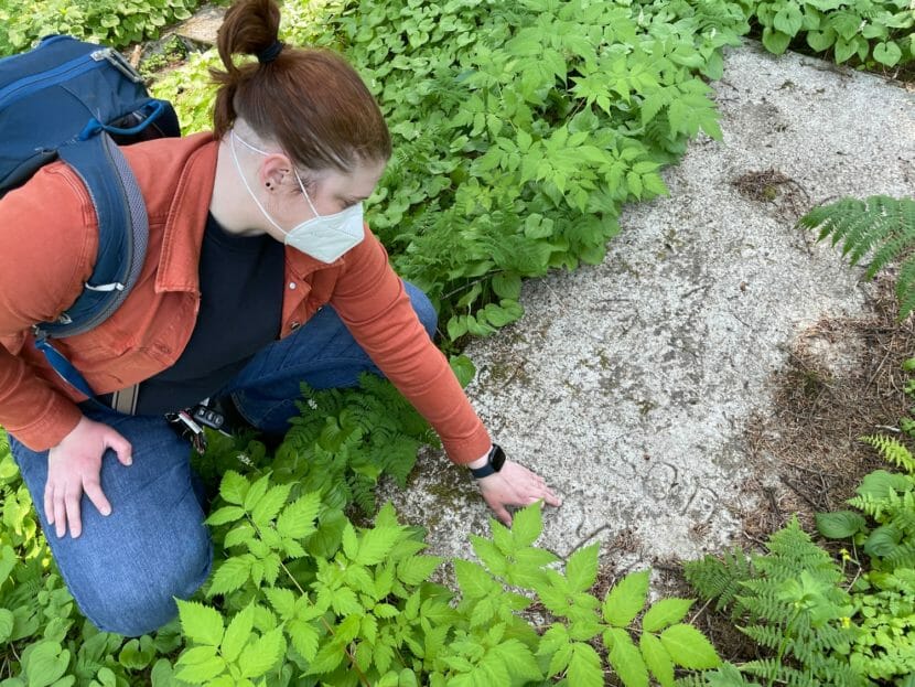 A woman wearing a mask kneels and brushes off a gravestone