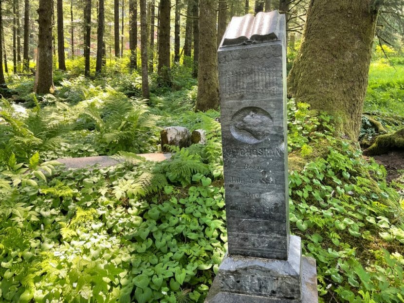 A tall tombstone with an intricate carving of a wolf's head,in a forest