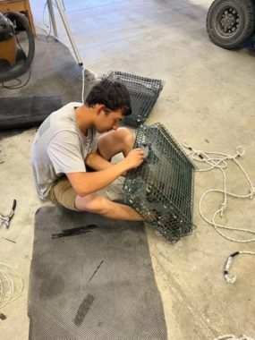 A man sits on a floor and works on a rectangular cage