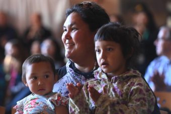 A smiling woman holds two small children, who are clapping
