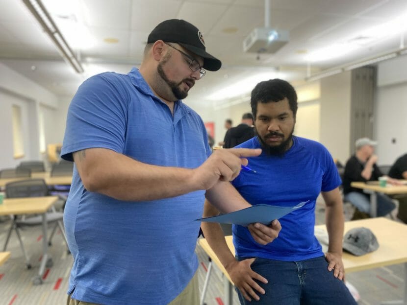 Two men in a classroom studying a piece of paper