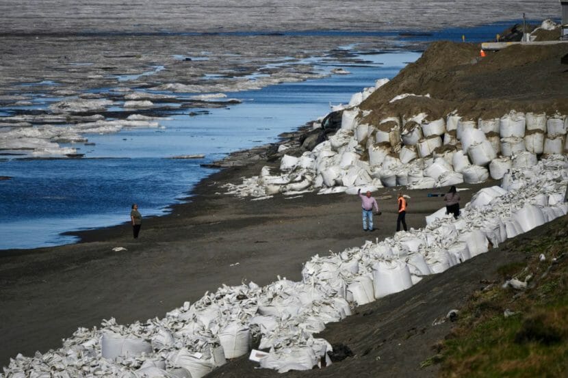 Four people on a beach, surrounded by part of a barrier made of large sandbags