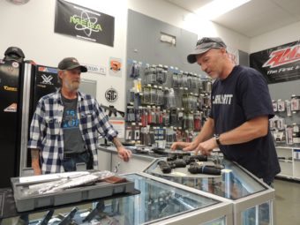 Two men on either side of a glass display case that has several pistols laid out on top of it
