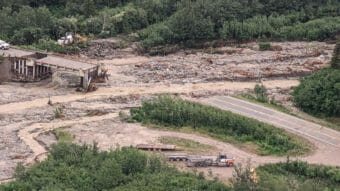 A photo from above showing a washed-out bridge and a muddy, swollen stream