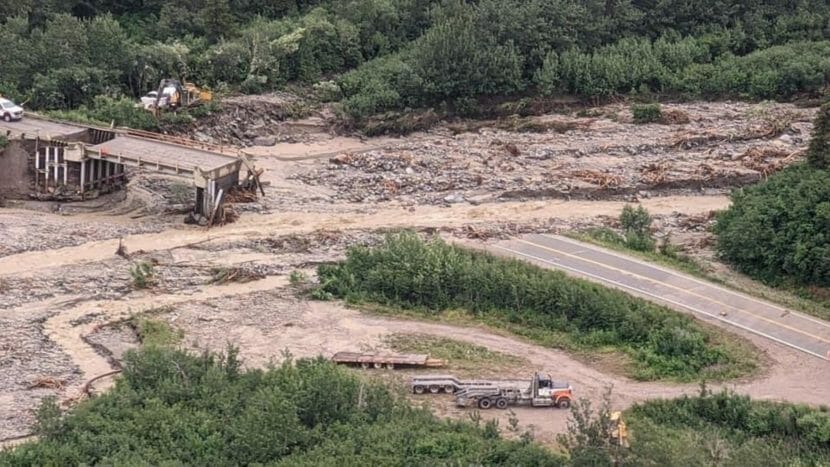 A photo from above showing a washed-out bridge and a muddy, swollen stream