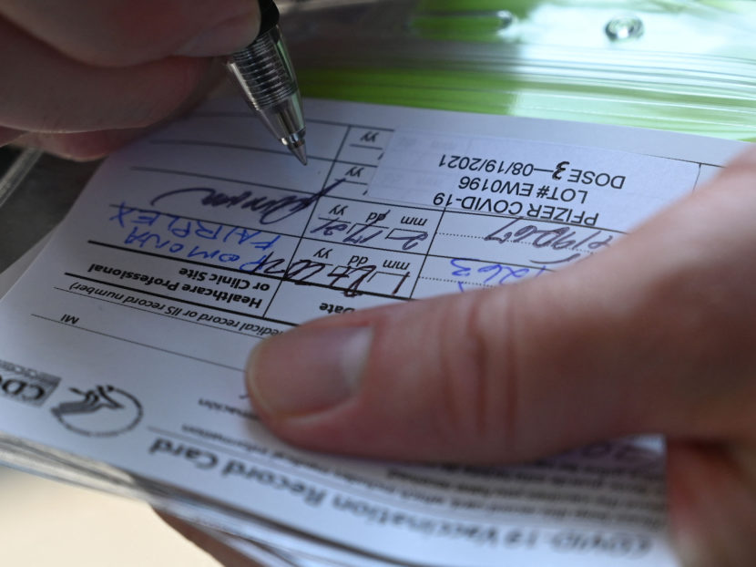 Fingers holding down and writing on a vaccination card