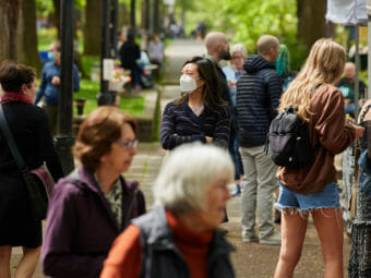 Shoppers in an outdoor market, one of them wearing a mask