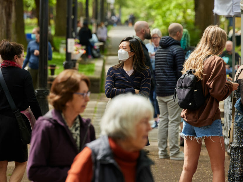 Shoppers in an outdoor market, one of them wearing a mask