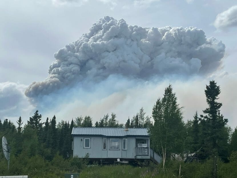 Wildfire smoke rising behind a house surrounded by trees.