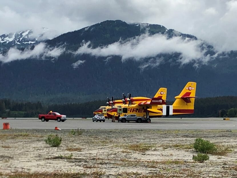 Bright yellow twin-prop airplanes that say fire in red letters on the side are parked on the ground with some trucks close by for scale.