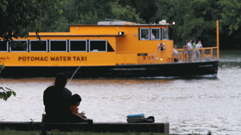 An orange river boat glides by an adult and child fishing from the bank