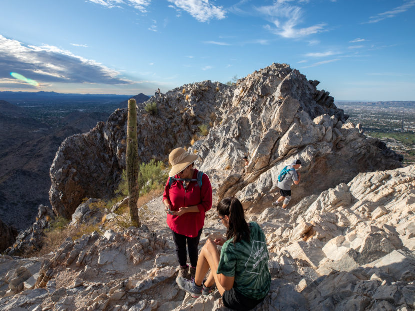 Two people next to a lone cactus on a rocky ridge