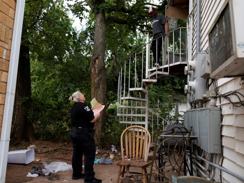 A police officer stands at the base of a spiral staircase talking to someone standing above.