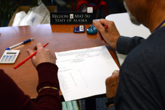 looking over the shoulders of two people marking a typed list with red pens