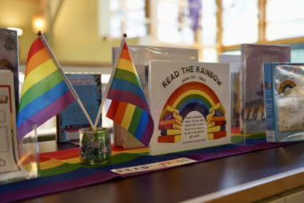 Small pride flags set up next to a "Read the Rainbow" library display