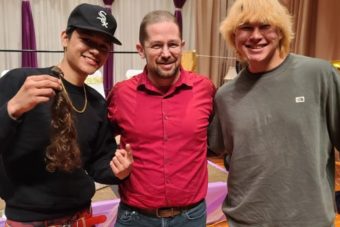 Two high school boys pose with a man with a shaven head