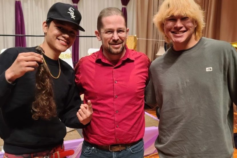 Two high school boys pose with a man with a shaven head