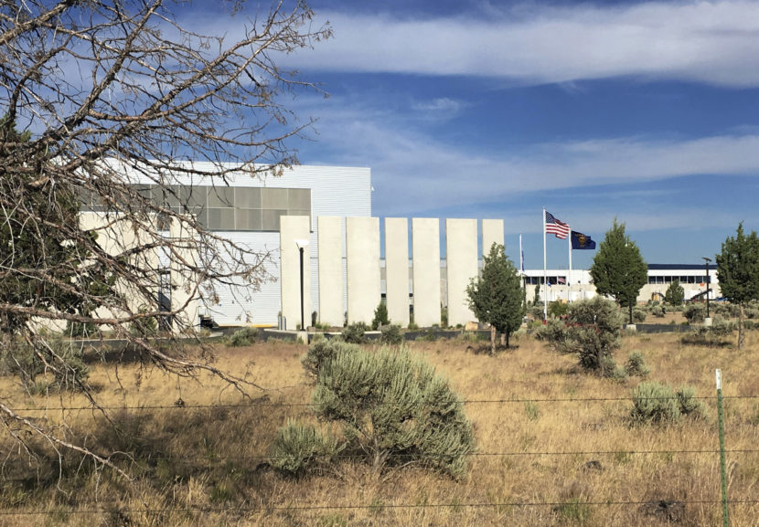 A large, non-descript building behind a barbed wire fence in an arid landscape 