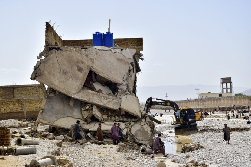 People and an excavator working around a completely ruined two-story building