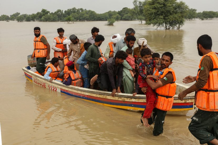 A skiff with about 15 people in it on a muddy, flooded river