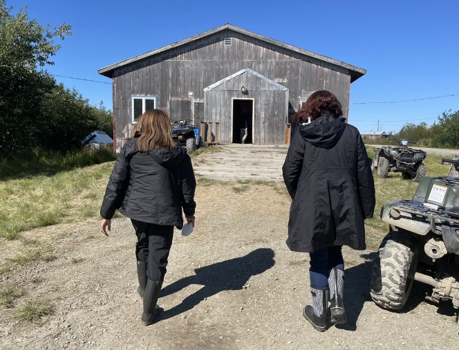 Two people walk toward a weathered wood house