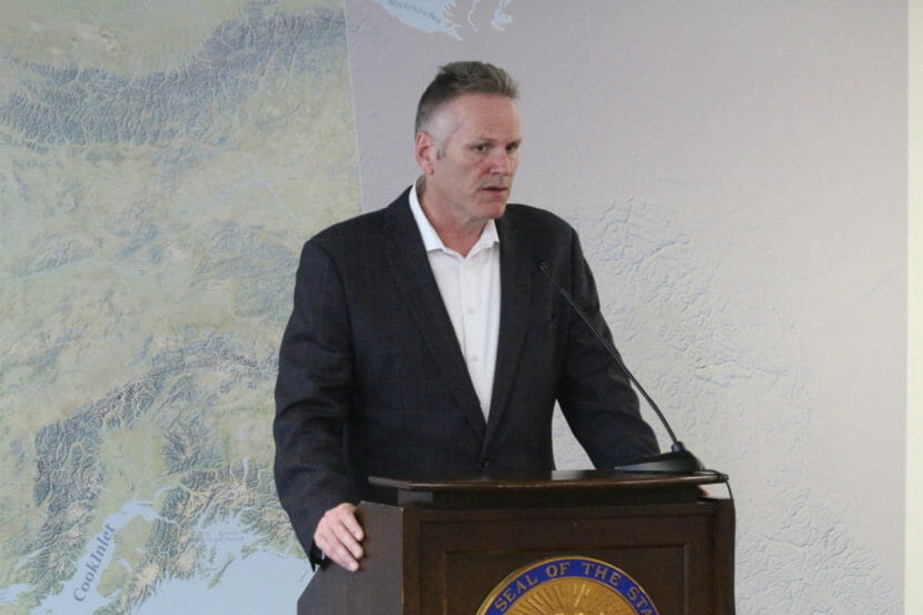 Gov. Dunleavy stands at a lectern in front of a map of Alaska