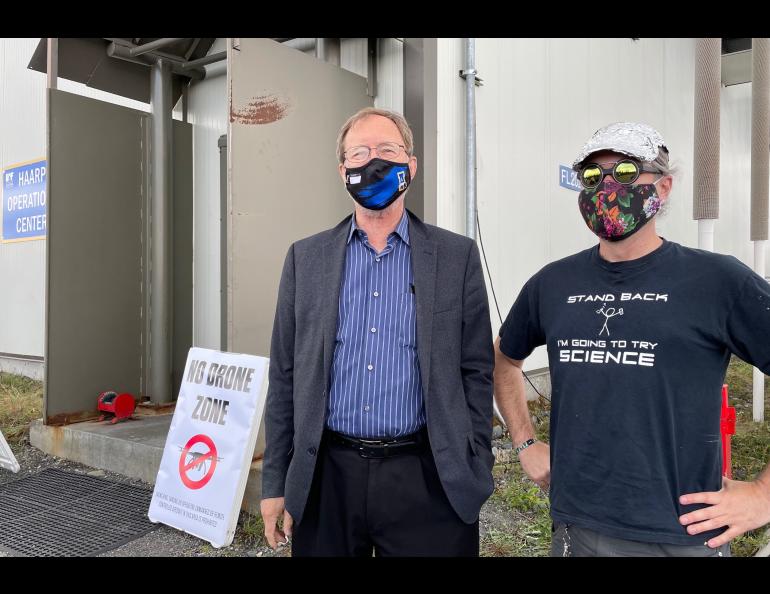 A man in a suit stands next to a man wearing a tinfoil hat