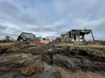 Two buildings at a fish camp, one badly damaged and the other knocked over