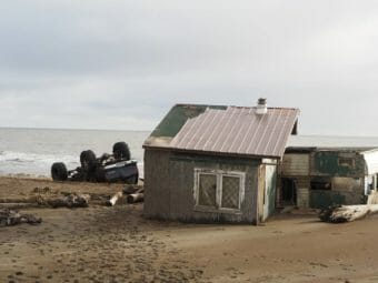A tilted, badly damaged camp with an upside-down truck lying next to it