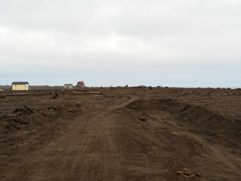 Tire tracks through a field of loose, recently deposited mud with small buildings in the background