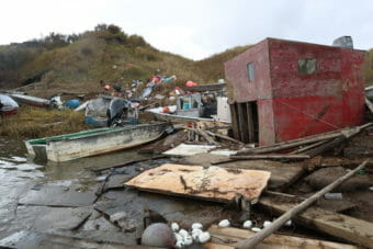 A small, square building, some skiffs, and fishing gear jumbled together onshore