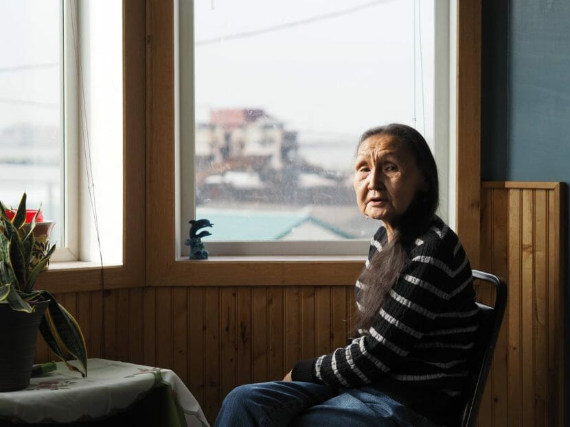 A woman sits at a table by a window overlooking Nome